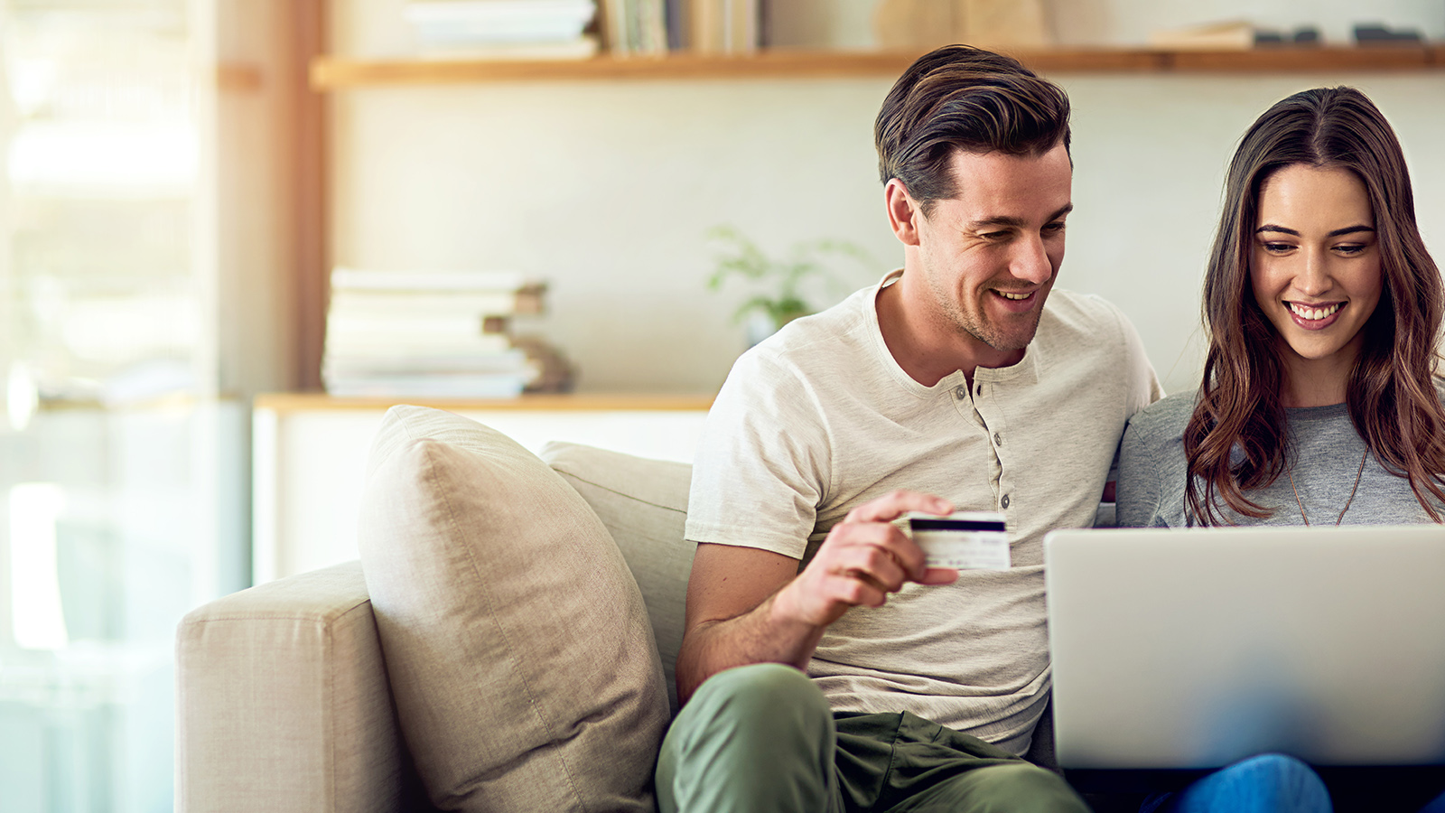 Happy couple at home paying bills with laptop and credit card