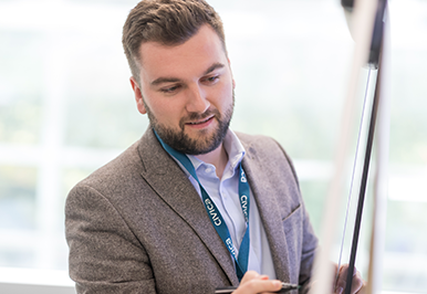 Close up of a young man writing on white board during a business project meeting