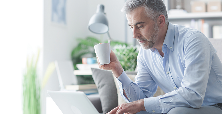 Man holding coffee mug and typing on a laptop