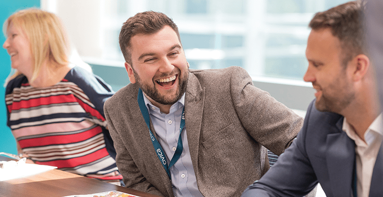 Smiling diverse businesspeople sit at office desk talk laugh discussing business ideas together