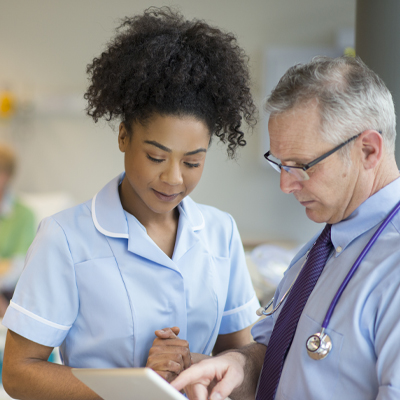 Doctor and nurse discussing over digital tablet in ward at hospital